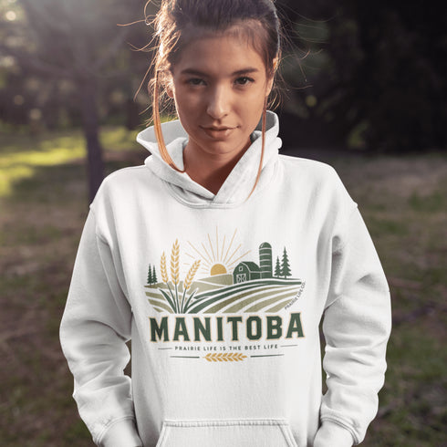 person wearing manitoba prairie life hoodie with farm and wheat field design standing in prairie field