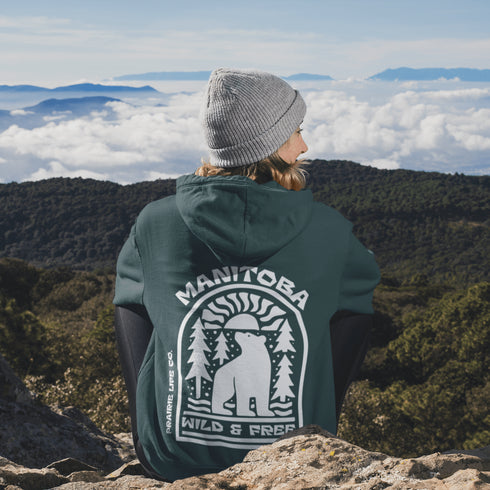 This cozy hoodie features a bold graphic of a bear surrounded by pine trees and rising sun—capturing the spirit of Manitoba’s rugged landscapes and Prairie Life culture.