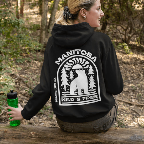 This cozy hoodie features a bold graphic of a bear surrounded by pine trees and rising sun—capturing the spirit of Manitoba’s rugged landscapes and Prairie Life culture.