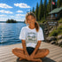 Woman sitting on a dock by a lake with a cabin and 'Falcon Lake Manitoba' sign in the background.