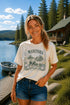 Woman wearing a Manitoba Canada wildlife graphic t-shirt featuring bears, wildflowers, forest landscape and lakeside cabin while standing on a dock at Falcon Lake Manitoba.