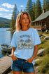 Woman wearing a Manitoba Canada wildlife graphic t-shirt featuring bears, wildflowers, forest landscape and lakeside cabin while standing on a dock at Falcon Lake Manitoba.
