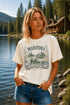 Woman wearing a Manitoba Canada wildlife graphic t-shirt featuring bears, wildflowers, forest landscape and lakeside cabin while standing on a dock at Falcon Lake Manitoba.