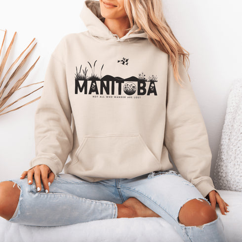 Featuring a prairie landscape, the design showcases wildflowers and prairie grasses blooming from the letters "Manitoba," artfully integrated into the scene.