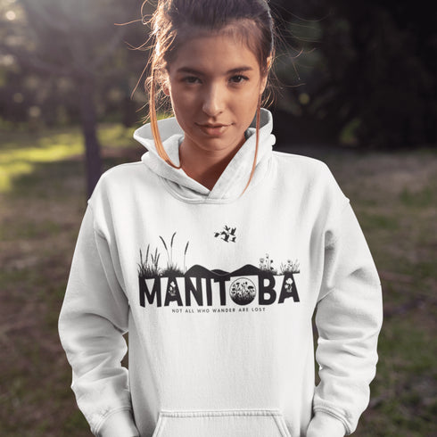 Featuring a prairie landscape, the design showcases wildflowers and prairie grasses blooming from the letters "Manitoba," artfully integrated into the scene.