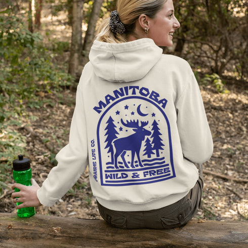 This Manitoba hoodie captures the beauty of Canada’s backcountry with a moose silhouette surrounded by starlit skies, tall evergreens, and a crescent moon.