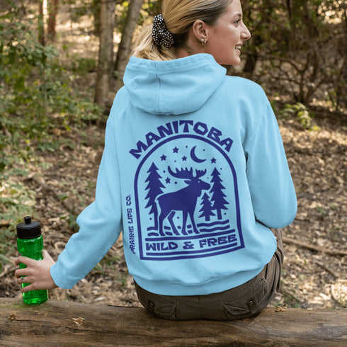 This Manitoba hoodie captures the beauty of Canada’s backcountry with a moose silhouette surrounded by starlit skies, tall evergreens, and a crescent moon.