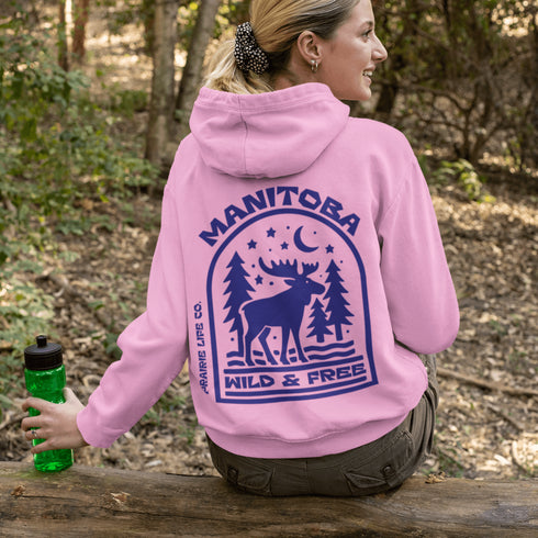 This Manitoba hoodie captures the beauty of Canada’s backcountry with a moose silhouette surrounded by starlit skies, tall evergreens, and a crescent moon.