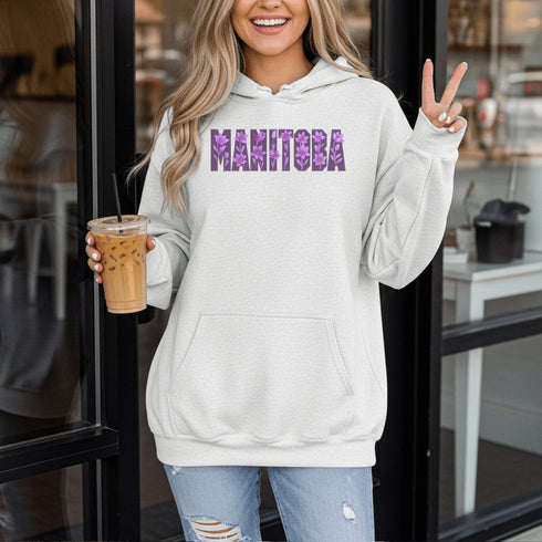 Celebrate the beauty of the prairies with our Manitoba Hoodie, featuring bold lettering filled with delicate purple prairie crocus flowers.