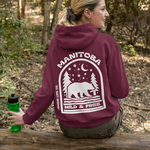 This cozy hoodie features a bold back print of a bear walking beneath a crescent moon and pine trees—capturing everything we love about Canada’s wilderness.