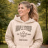Woman wearing beige Maple Syrup Fan Club hoodie with maple leaf graphic, smiling outdoors in a natural setting with trees in the background