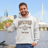 Man wearing a Maple Syrup Fan Club hoodie with maple leaf graphic, smiling outdoors in a natural setting with trees in the background