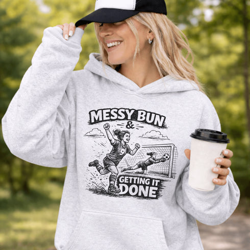 Woman wearing a Messy Bun & Getting It Done soccer mom hoodie with vintage soccer design, holding coffee outdoors