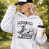 Woman wearing a Messy Bun & Getting It Done soccer mom hoodie with vintage soccer design, holding coffee outdoors