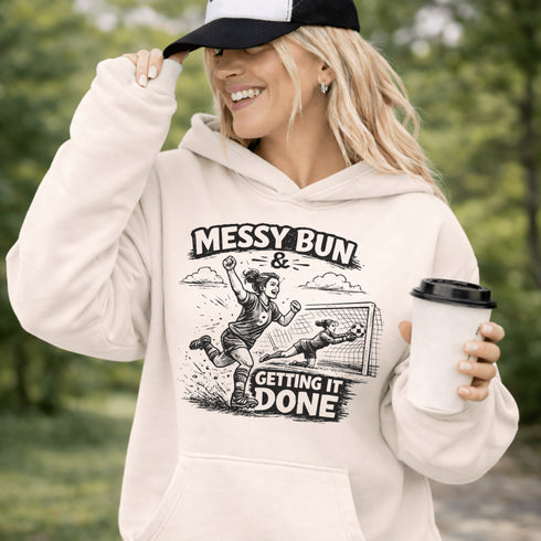 Woman wearing a Messy Bun & Getting It Done soccer mom hoodie with vintage soccer design, holding coffee outdoors