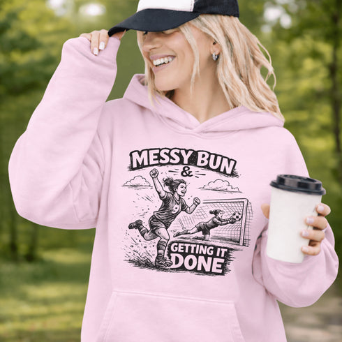 Woman wearing a Messy Bun & Getting It Done soccer mom hoodie with vintage soccer design, holding coffee outdoors