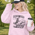 Woman wearing a Messy Bun & Getting It Done soccer mom hoodie with vintage soccer design, holding coffee outdoors