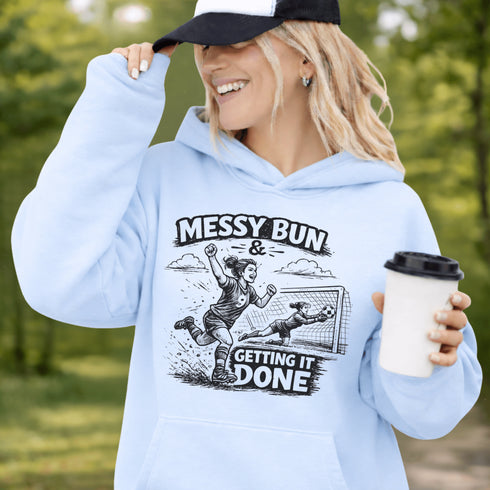 Woman wearing a Messy Bun & Getting It Done soccer mom hoodie with vintage soccer design, holding coffee outdoors