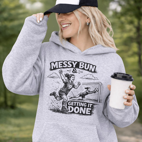Woman wearing a Messy Bun & Getting It Done soccer mom hoodie with vintage soccer design, holding coffee outdoors