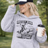 Woman wearing a Messy Bun & Getting It Done soccer mom hoodie with vintage soccer design, holding coffee outdoors