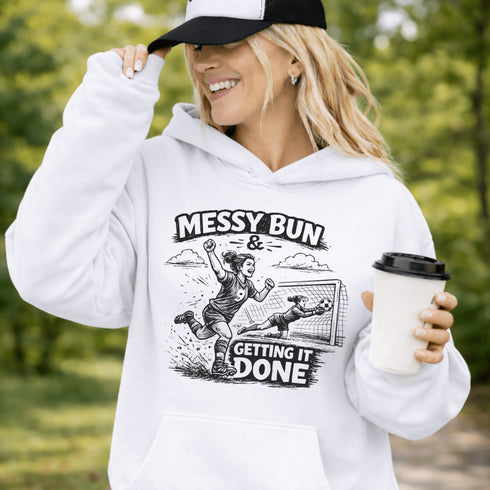 Woman wearing a light blue Messy Bun & Getting It Done soccer mom hoodie with vintage soccer design, holding coffee outdoors