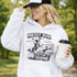 Woman wearing a light blue Messy Bun & Getting It Done soccer mom hoodie with vintage soccer design, holding coffee outdoors