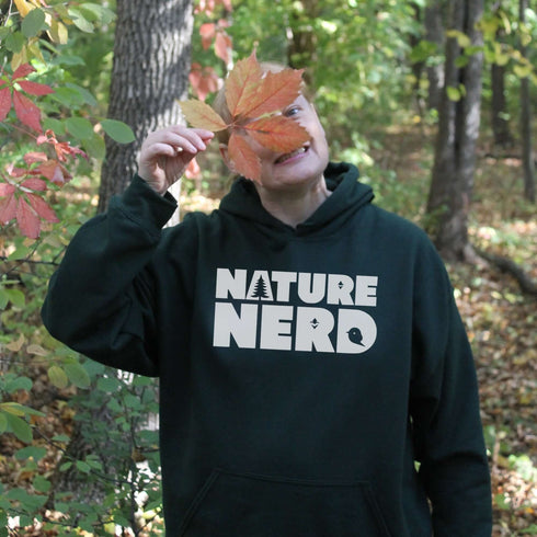Person wearing a 'Nature Nerd' hoodie holding a leaf in front of their face outdoors.