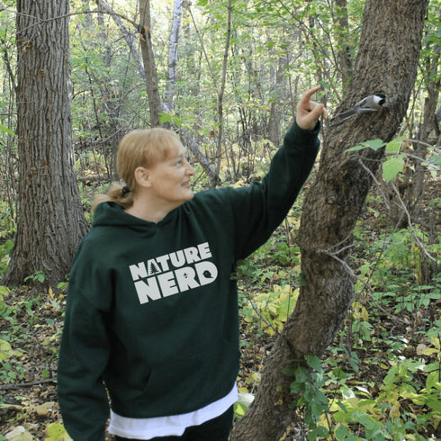 Person wearing a 'Nature Nerd' hoodie interacting with a bird in a forest.