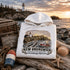 White hoodie with New Brunswick design on a coastal background with lighthouse and ocean.