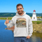 Man wearing a hoodie with New Brunswick design, standing in front of a lighthouse and lake.