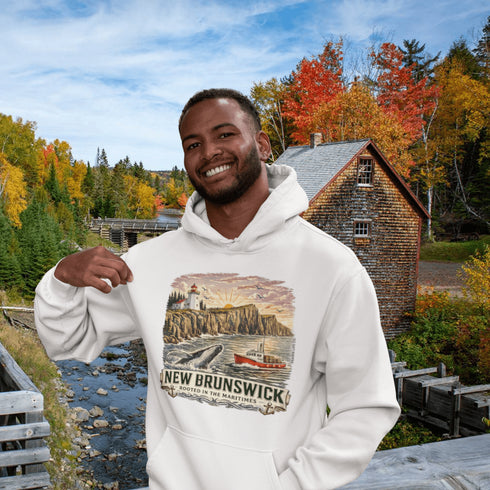 Man wearing a white hoodie with New Brunswick design in front of a scenic autumn landscape.