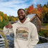 Man wearing a hoodie with New Brunswick design in front of a scenic autumn landscape.