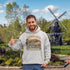 Man wearing a hoodie with a New Brunswick design in front of a windmill.