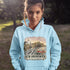 Person wearing a light blue hoodie with a New Brunswick design outdoors.