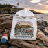 White hoodie with New Brunswick design on a rocky coastal background with lighthouse.