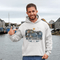 Man wearing a hoodie with a 'Newfoundland' design by a waterfront.