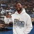 Man wearing a white hoodie with a 'Newfoundland' design, standing in front of a scenic background.