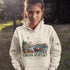 Nova Scotia hoodie with lighthouse coastal fishing village graphic worn by model outdoors near ocean cliffs