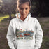 Nova Scotia hoodie with lighthouse coastal fishing village graphic worn by model outdoors near ocean cliffs