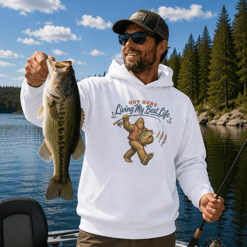 Unisex Gildan 18500 hoodie featuring a vintage-style Bigfoot fishing graphic with the phrase "Out Here Living My Best Life," available in multiple colors.
