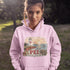 Person wearing a pink hoodie with a lighthouse design and 'PEI' text outdoors.