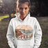 Person wearing a white hoodie with a scenic design and 'PEI' text outdoors.