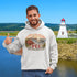Man wearing a hoodie with PEI design in front of a lighthouse and lake.