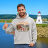 Man wearing a hoodie with a lighthouse design and 'PEI' text, standing in front of a scenic background.