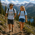 Two hikers on a mountain trail with scenic mountains and lake in the background