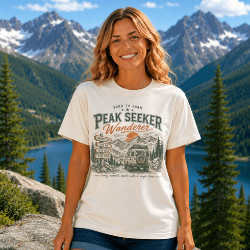 Woman wearing a 'Wander Far' t-shirt with a scenic mountain design, standing in front of a lake and mountains.