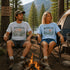 Two people sitting by a campfire in a forest with 'Peak Seeker' and 'Wander Far' t-shirts.