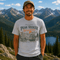 Man wearing Peak Seeker Wanderer mountain adventure graphic t-shirt featuring vintage mountain landscape, forest scenery, overland vehicle artwork, and retro outdoor design.