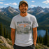 Man wearing Peak Seeker Wanderer mountain adventure graphic t-shirt featuring vintage mountain landscape, forest scenery, overland vehicle artwork, and retro outdoor design.