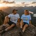 Two people sitting on a mountain top with scenic view and 'Peak Seeker' t-shirts.